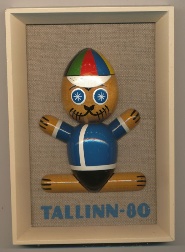 Ein hölzernes Spielzeug mit einer blauen und roten Mütze, beschriftet mit "Tallinn-80", in einem weißen Rahmen.