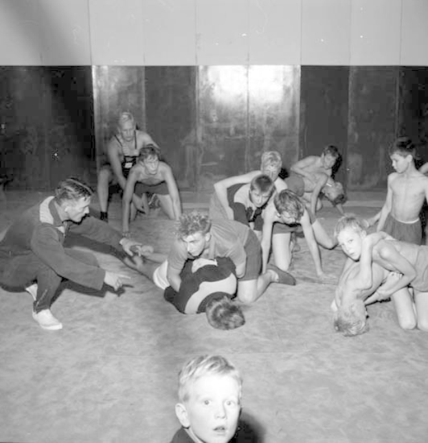 Schwarzes und weißes Foto von jungen Jungs, die in einer Turnhalle ringen, mit einer Wand im Hintergrund.