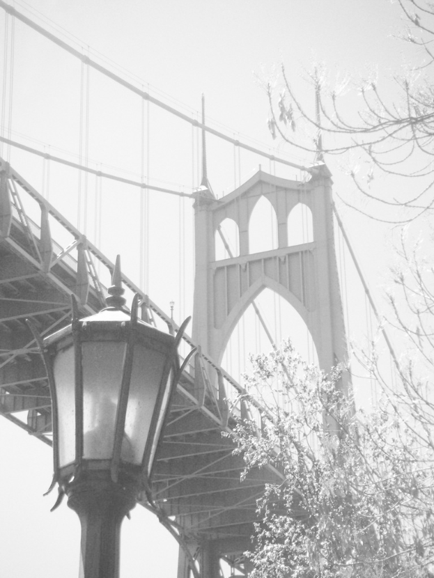 Ein altes Bild einer Hängebrücke mit einem schwarzen Laternenmast im Vordergrund und einem Baum in der rechten Ecke.
