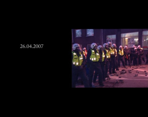 Eine Gruppe von Polizisten in Helmen und Jacken steht vor einem Gebäude mit Fenstern, mit einem Datum auf der linken Seite des Bildes.