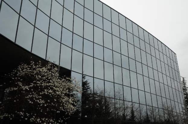 Ein modernes Gebäude mit Glasfront, umgeben von Bäumen, unter einem klaren Himmel.