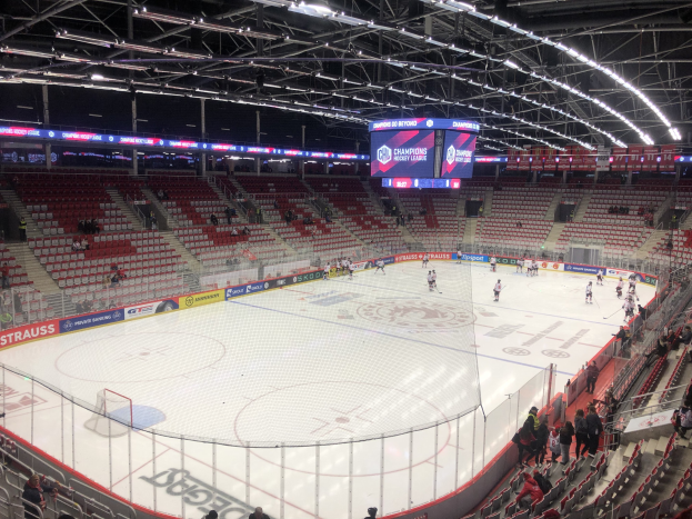 Ein Eishockeyspiel in einer großen Arena mit Zuschauern auf Sitzplätzen und Stehplätzen, einem Zaun um die Eisfläche, einem Bildschirm mit der Anzeige "St. Louis Blues vs Detroit Red Wings", Metallrahmen und einer Decke mit Deckenbeleuchtung.