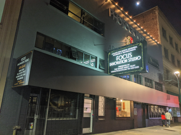 Außenansicht des Focus Innovation Studio in New York City bei Nacht, mit beleuchteten Gebäuden, Passanten auf dem Gehweg und sichtbarem Himmel im Hintergrund.